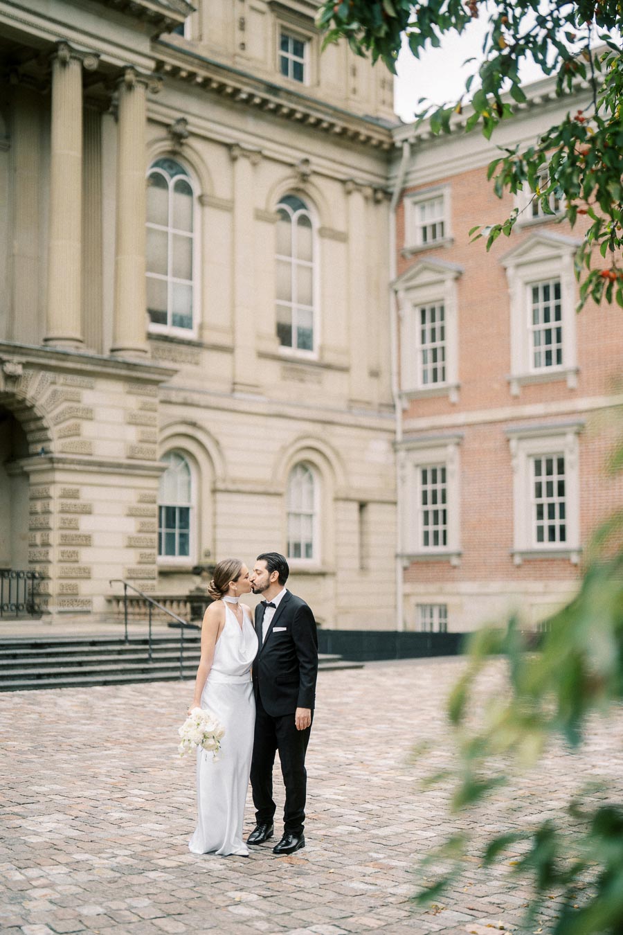 Elegant couple sharing a romantic kiss in front of historic building with classical architecture.
