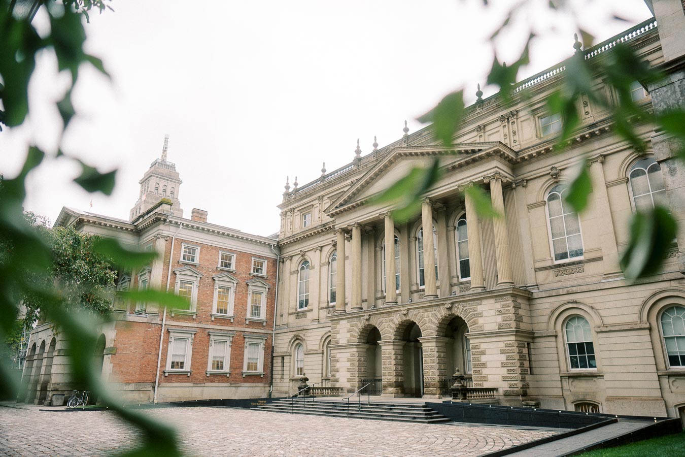 Historic courthouse with neoclassical architecture, featuring tall columns and arched windows, framed by green leaves in the foreground.