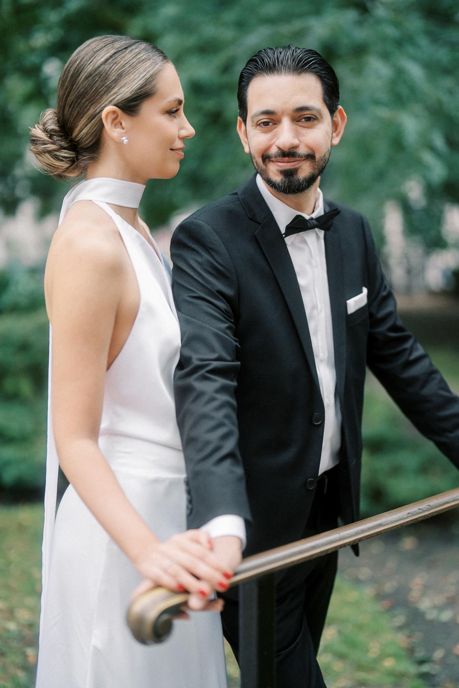 Wedding couple posing outdoors, with the groom in a black tuxedo and the bride in a white gown.