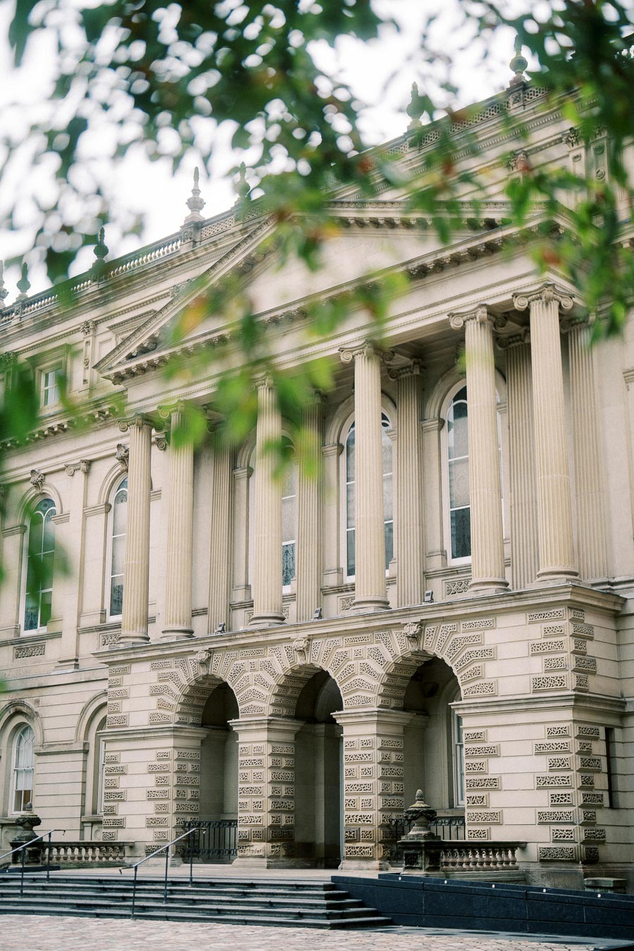 Historic neoclassical building with ornate columns and arches, surrounded by greenery.