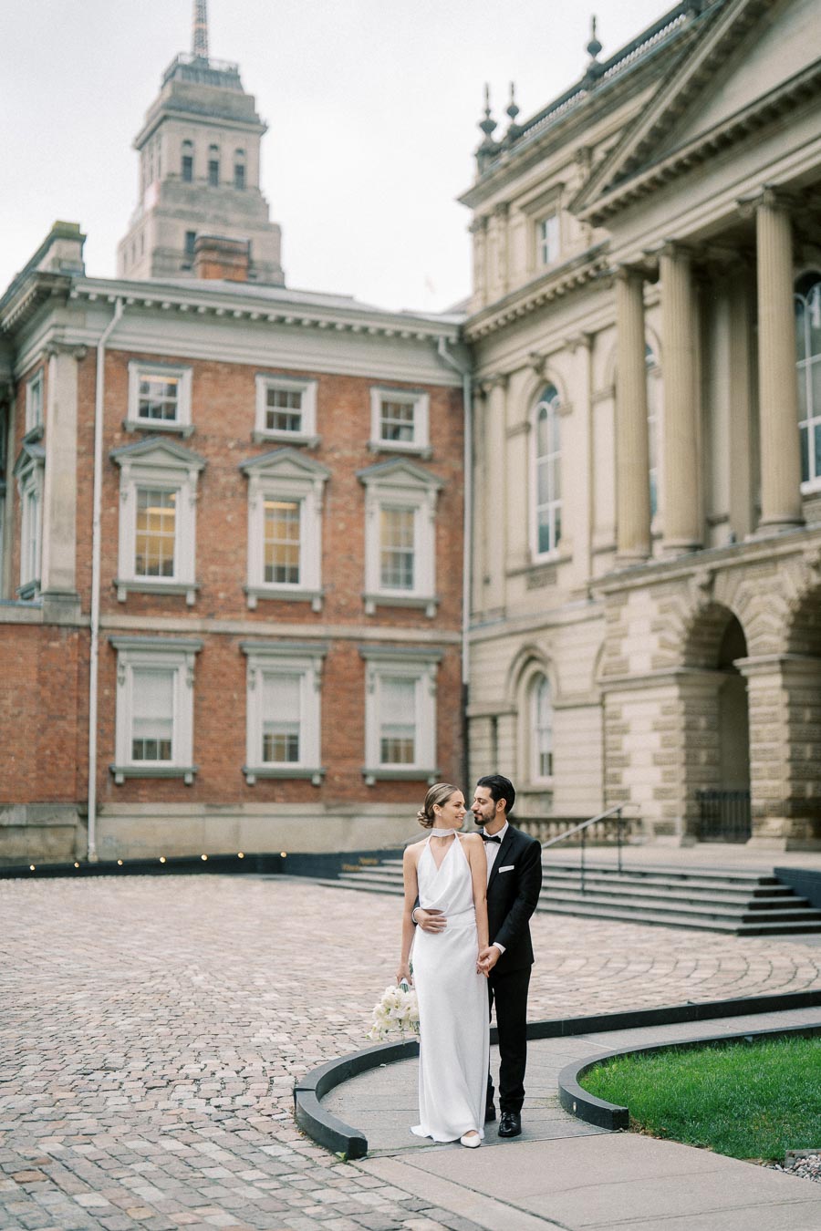 Elegant Couple Posing in Front of Historic Building on Cobblestone Courtyard During Wedding Photo Shoot