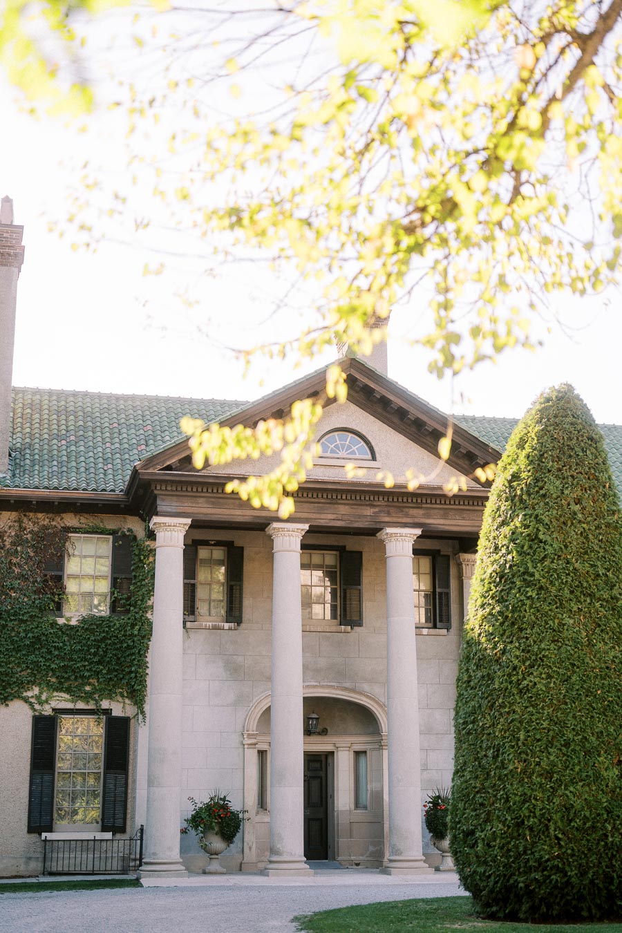 Elegant historic mansion with grand columns and ivy-covered facade, surrounded by lush greenery and a manicured garden.