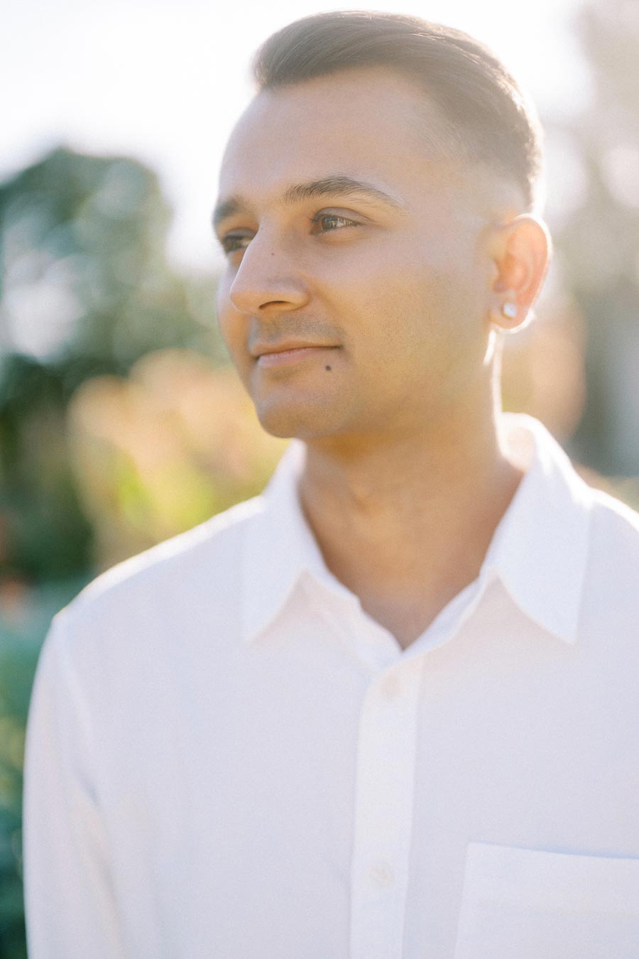 Portrait of a person in a white shirt, outdoors, with soft natural lighting and a blurred background of greenery.