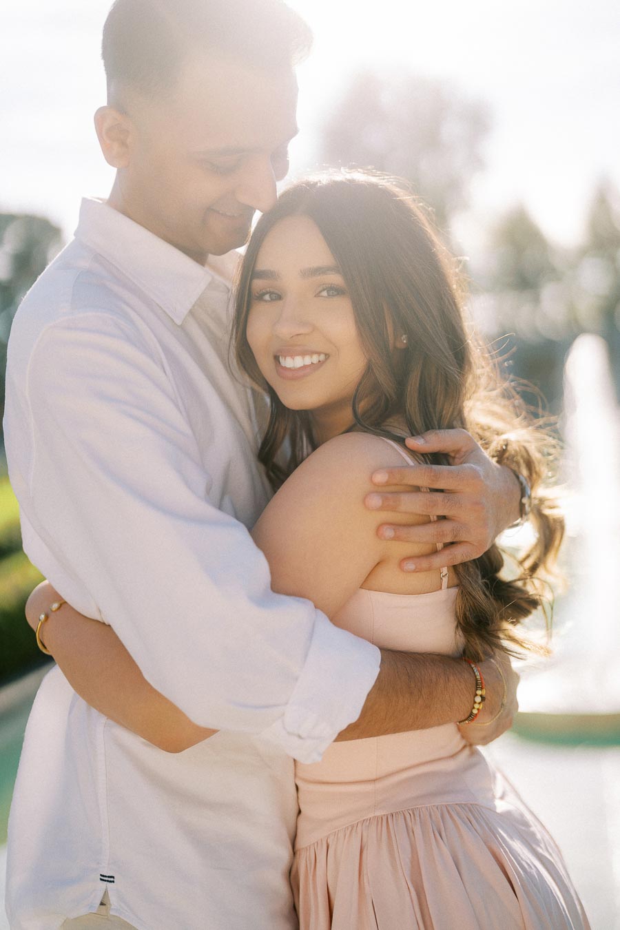 Smiling couple embracing outdoors in sunlight, highlighting romance and happiness.
