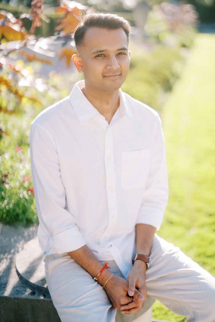 A person in a white shirt sitting on a garden bench in sunlight, surrounded by greenery and autumn leaves.