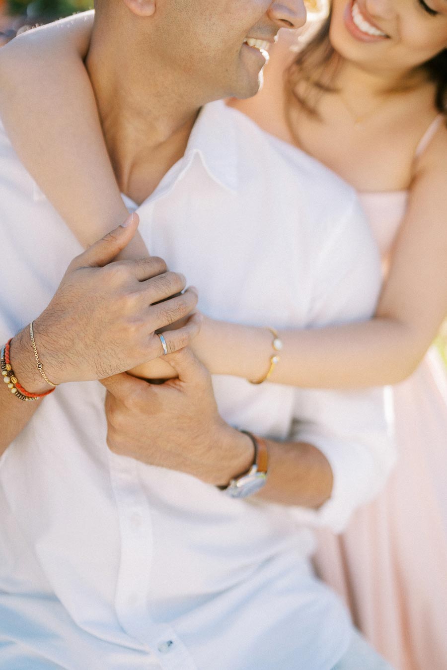 Smiling couple embracing, focused on hands with wedding ring and bracelets, conveying love and togetherness.
