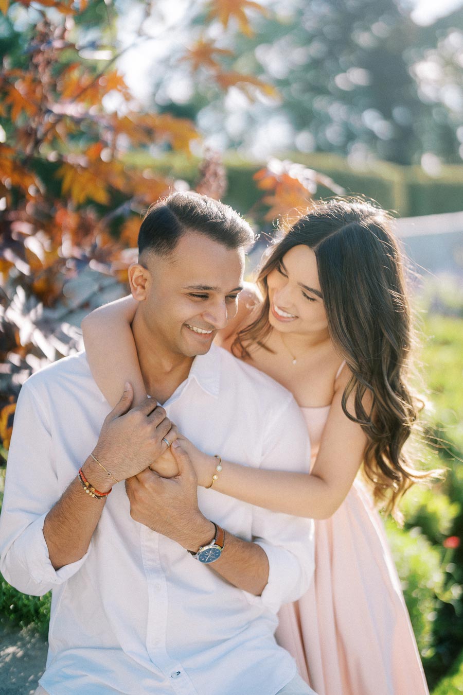 A happy couple embracing in a garden setting with colorful autumn leaves in the background.