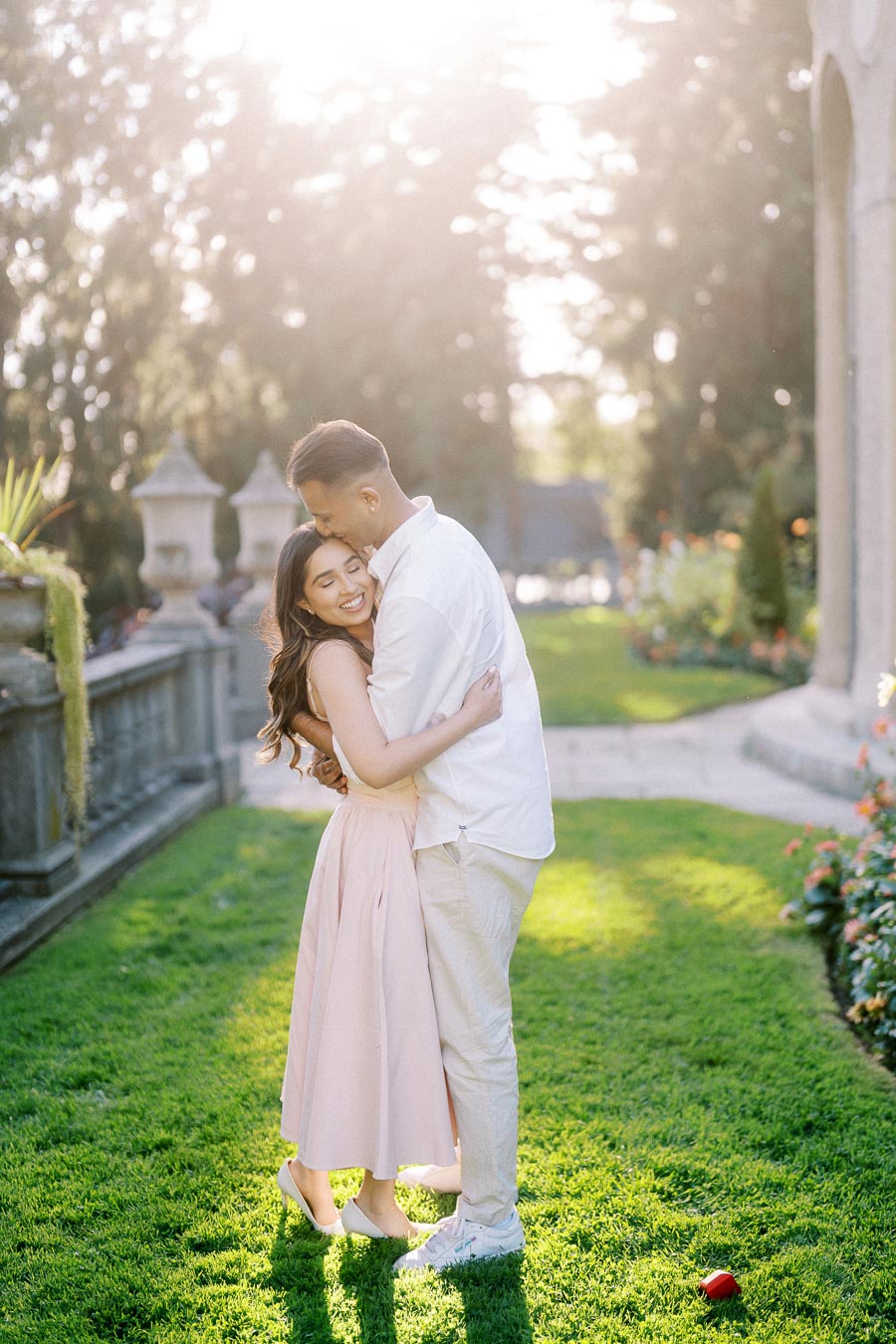 A romantic couple embracing in a sunlit garden, surrounded by greenery and flowers, with a soft glow highlighting their happiness.