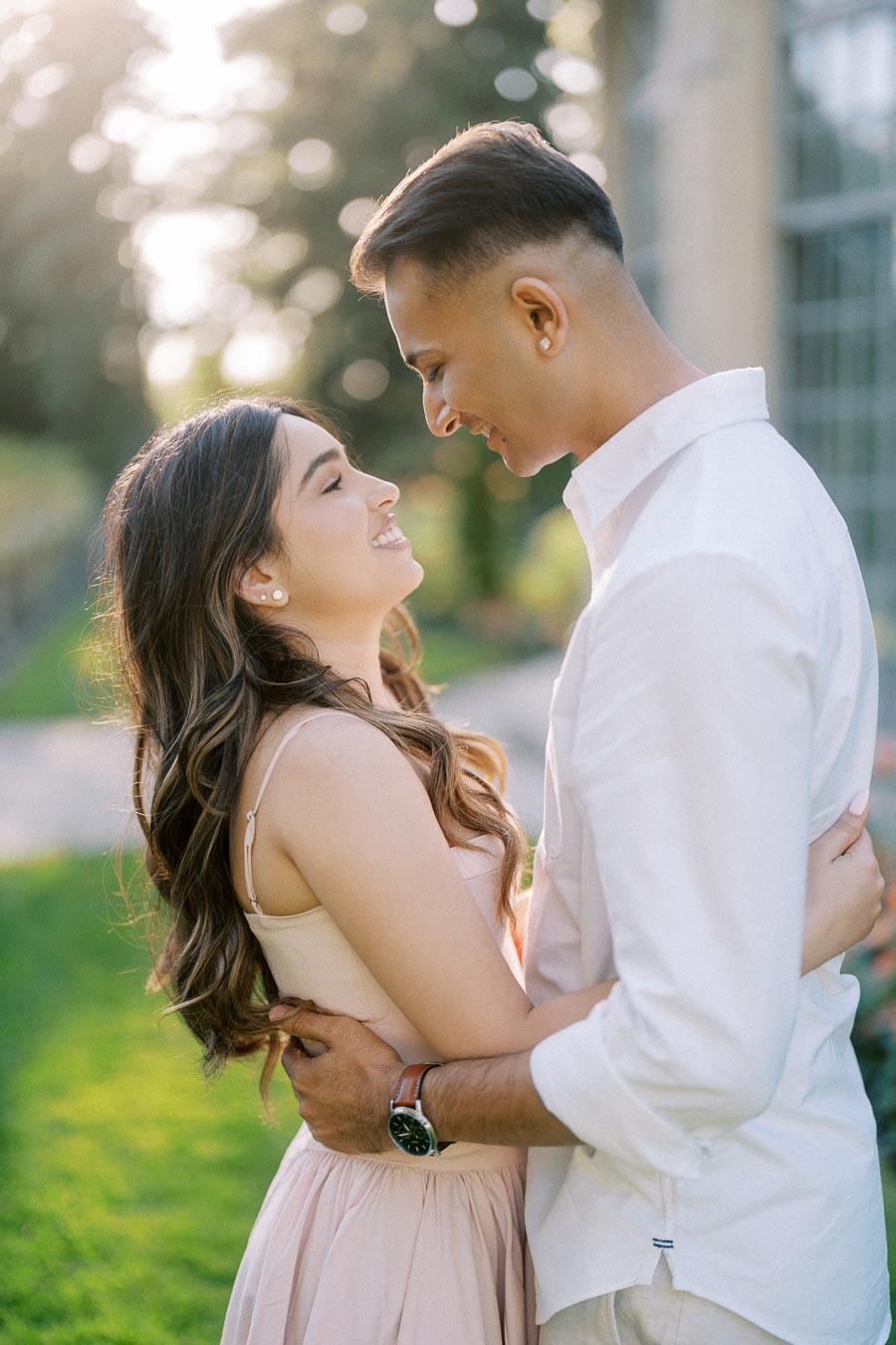 A young couple smiling and embracing each other in a sunlit garden, showcasing love and happiness.