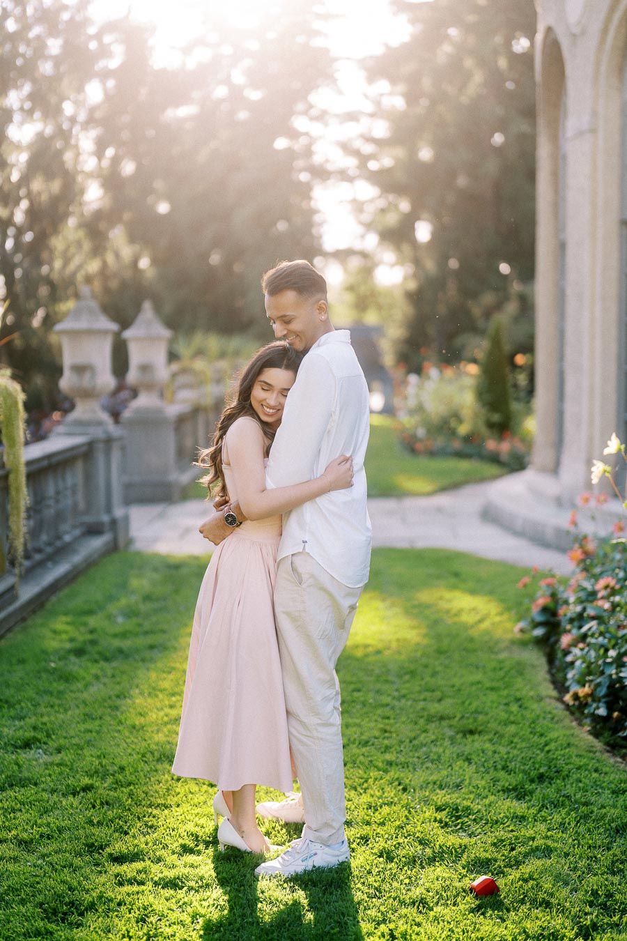 A happy couple embracing in a sunlit garden setting, surrounded by lush green grass and blooming flowers, creating a romantic atmosphere.