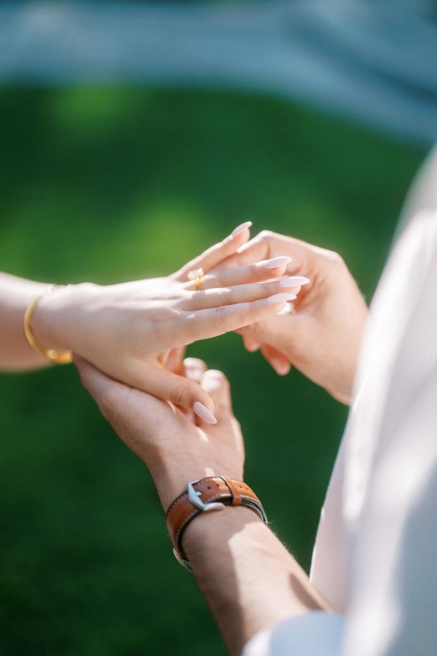 Close-up of two hands with a person placing a gold engagement ring on another person's finger, symbolizing love and commitment.