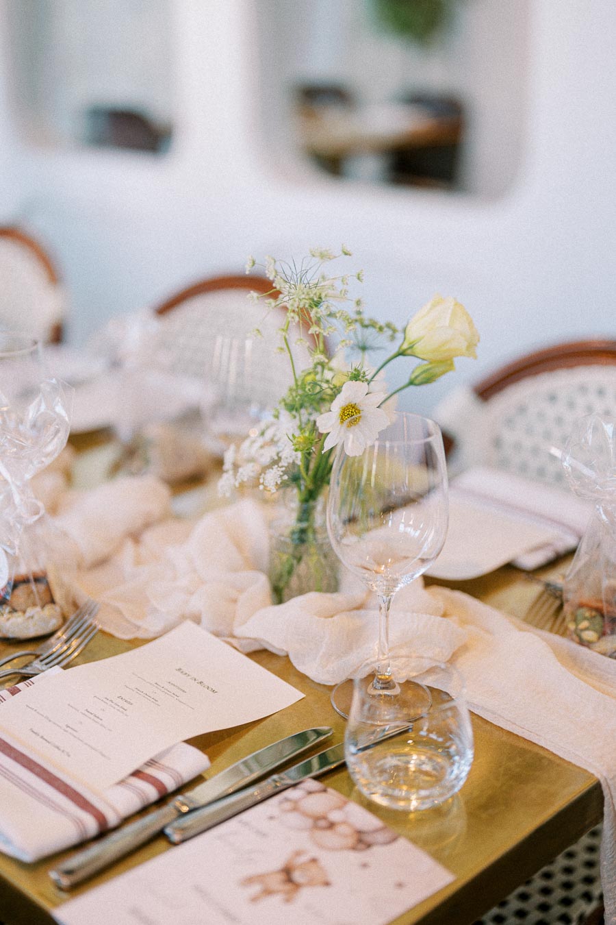 Elegant dining table setting with a floral centerpiece, wine glasses, and a menu displayed on a gold table, creating a sophisticated atmosphere for a special event or wedding reception.