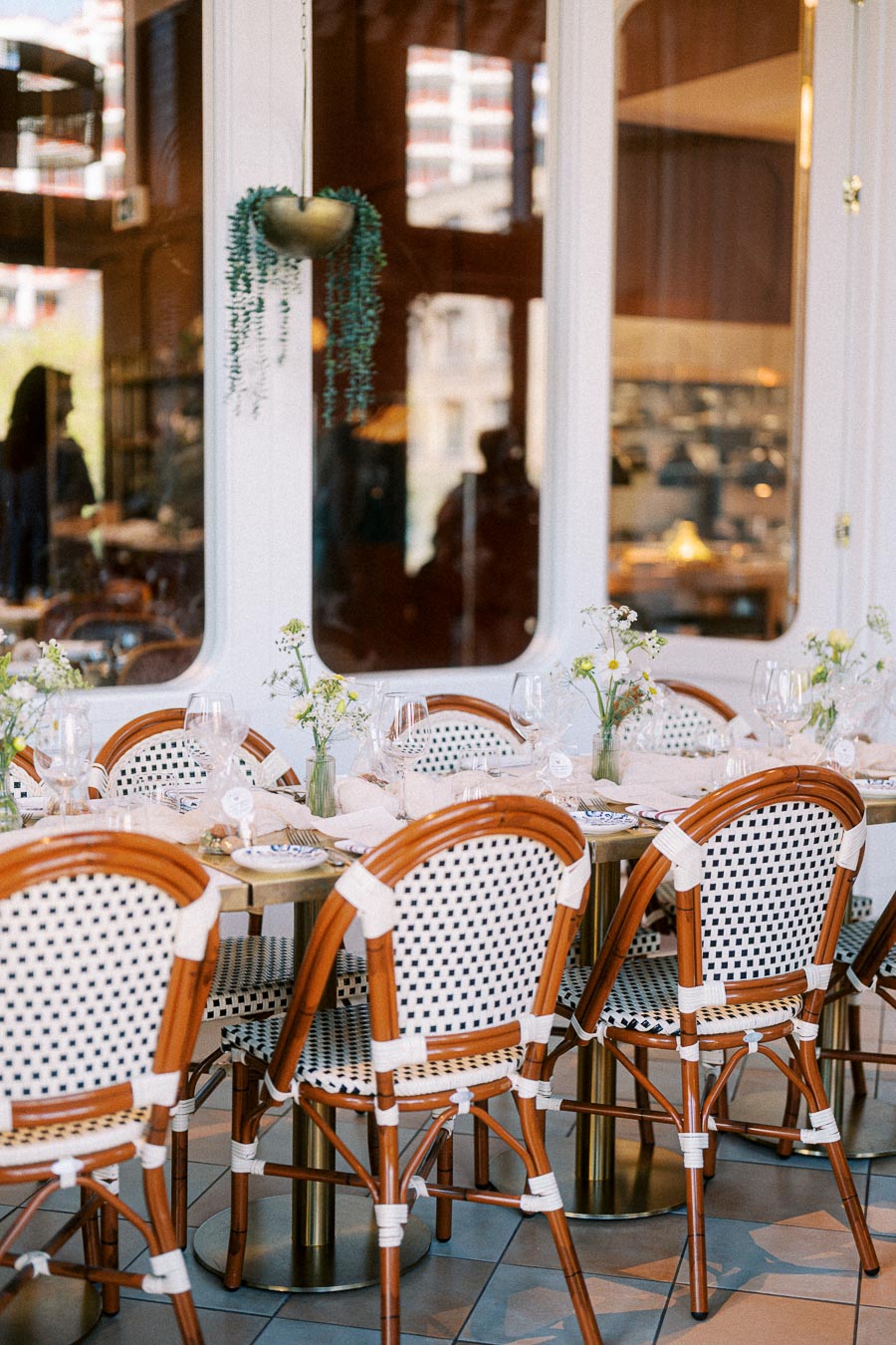 Elegant restaurant setting with woven bistro chairs around a table decorated with flowers and wine glasses, showcasing an inviting dining atmosphere with warm natural lighting.
