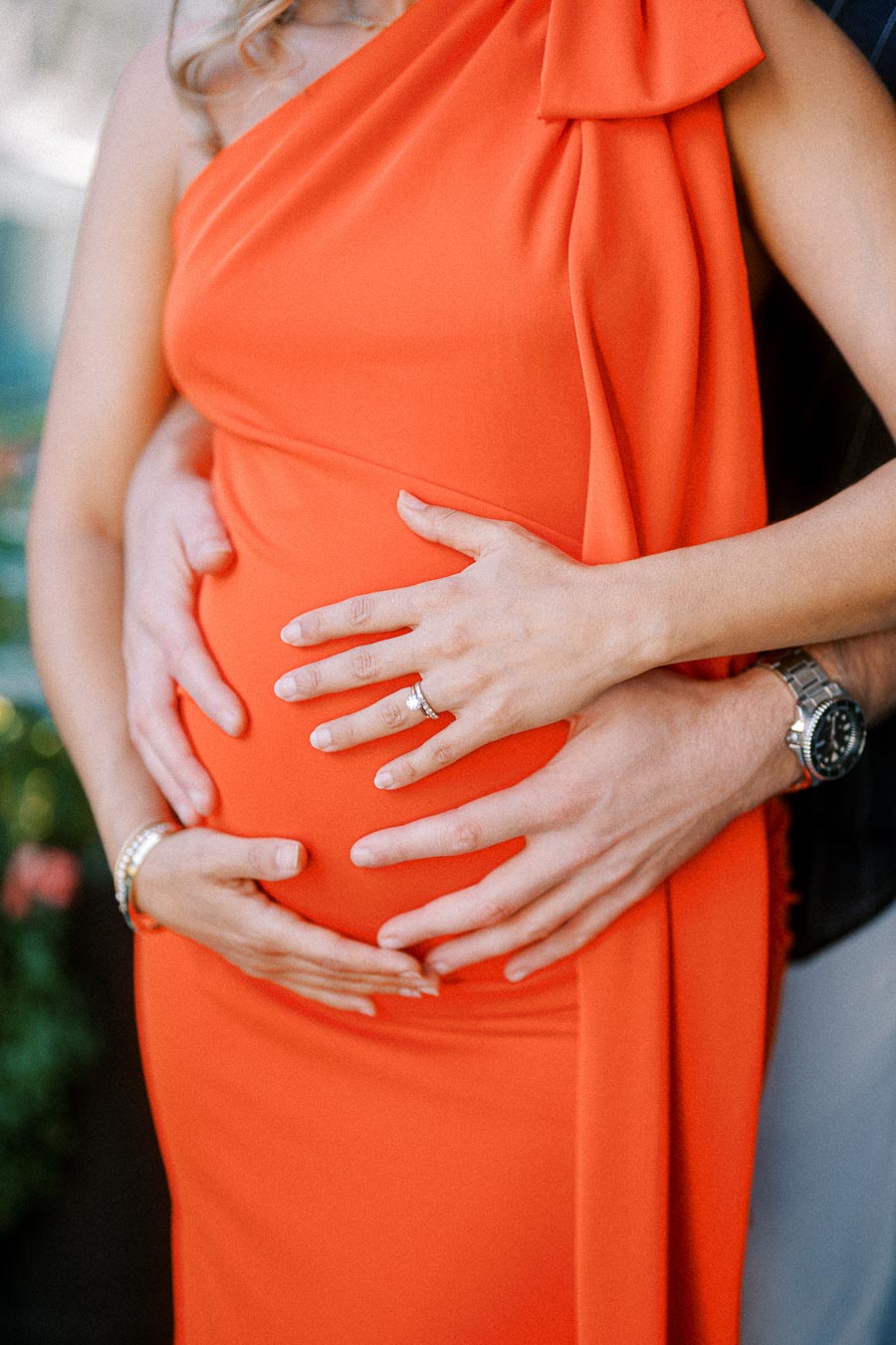 Pregnant woman in an elegant orange dress with hands gently cradling her belly, symbolizing love and anticipation.