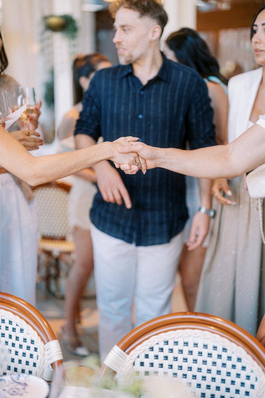 People shaking hands at a social gathering, surrounded by others conversing and holding drinks, highlighting networking and connection in a relaxed setting.