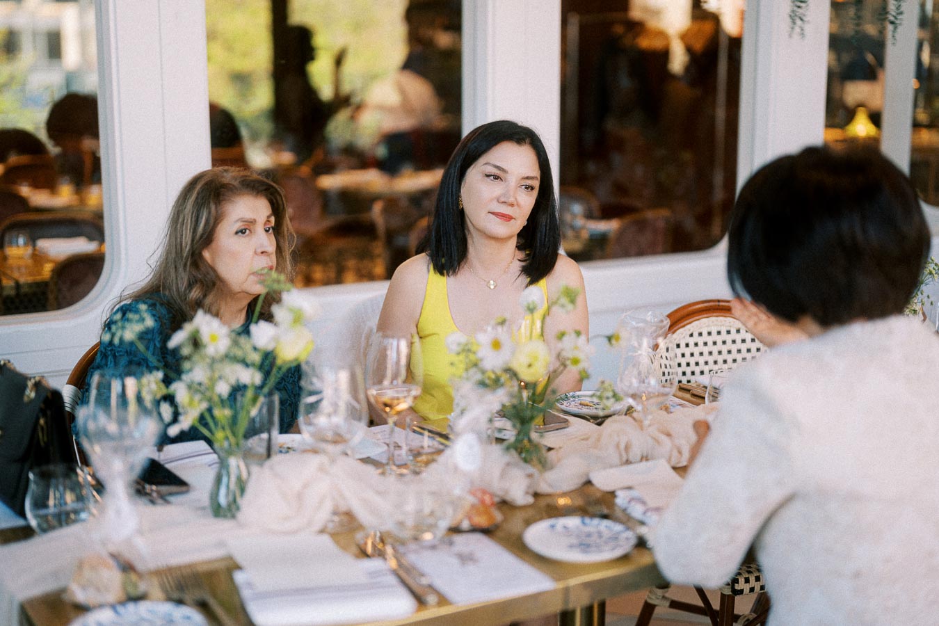 Women having a conversation at a beautifully set dining table in a restaurant, featuring elegant tableware and a floral centerpiece.