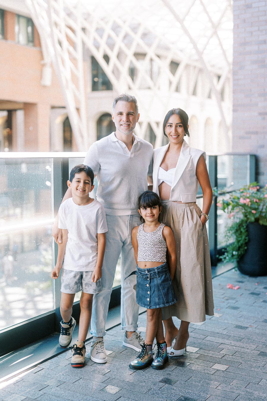 Family enjoying a day out in a modern architectural setting, with a man and woman standing behind two smiling children on a sunlit outdoor terrace.