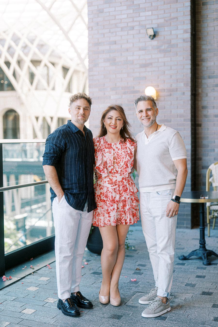 A group of three people posing happily together on a stylish outdoor patio, with modern architectural elements in the background.