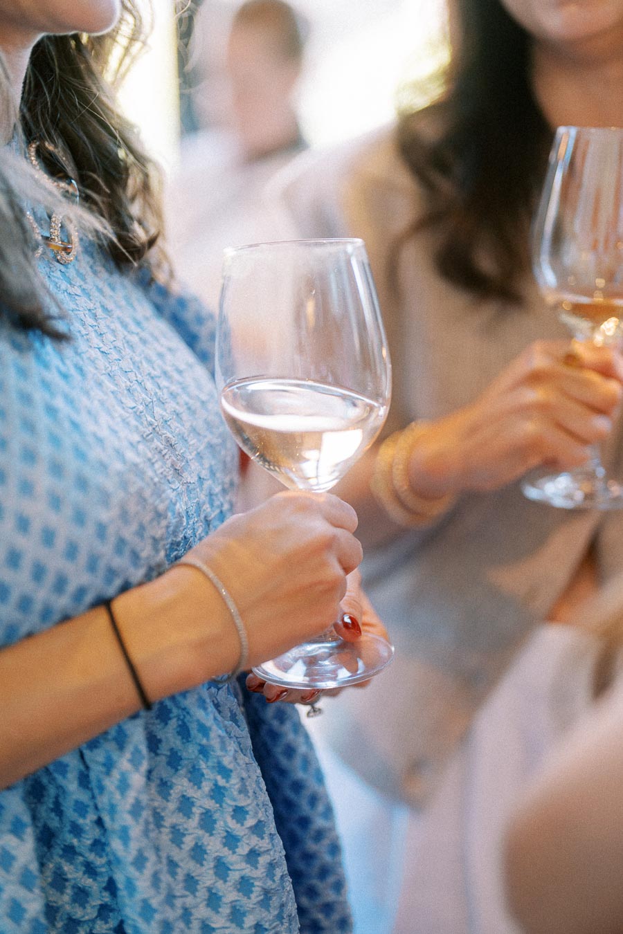 Two women holding wine glasses at an upscale event, focusing on their elegant attire and jewelry, creating a sophisticated and social atmosphere.
