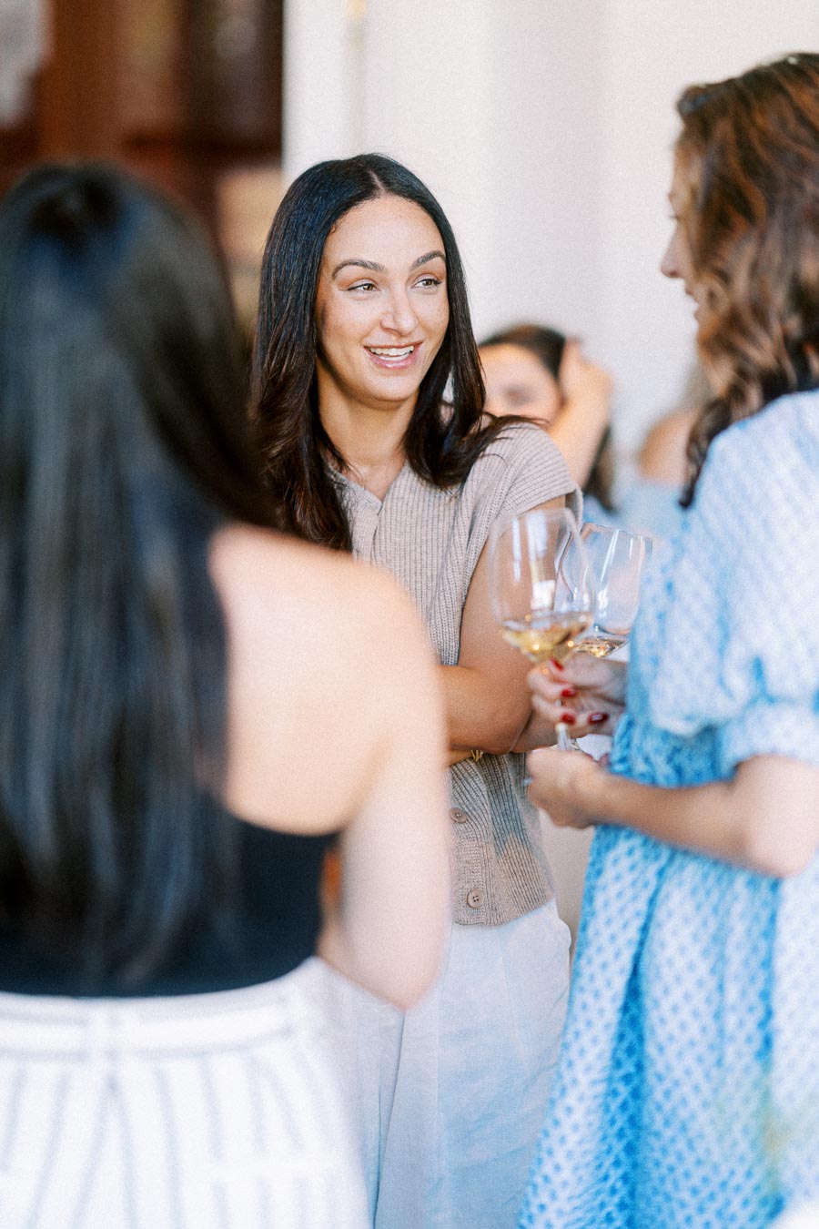 Group of casually dressed women engaged in conversation and holding wine glasses at a social gathering.