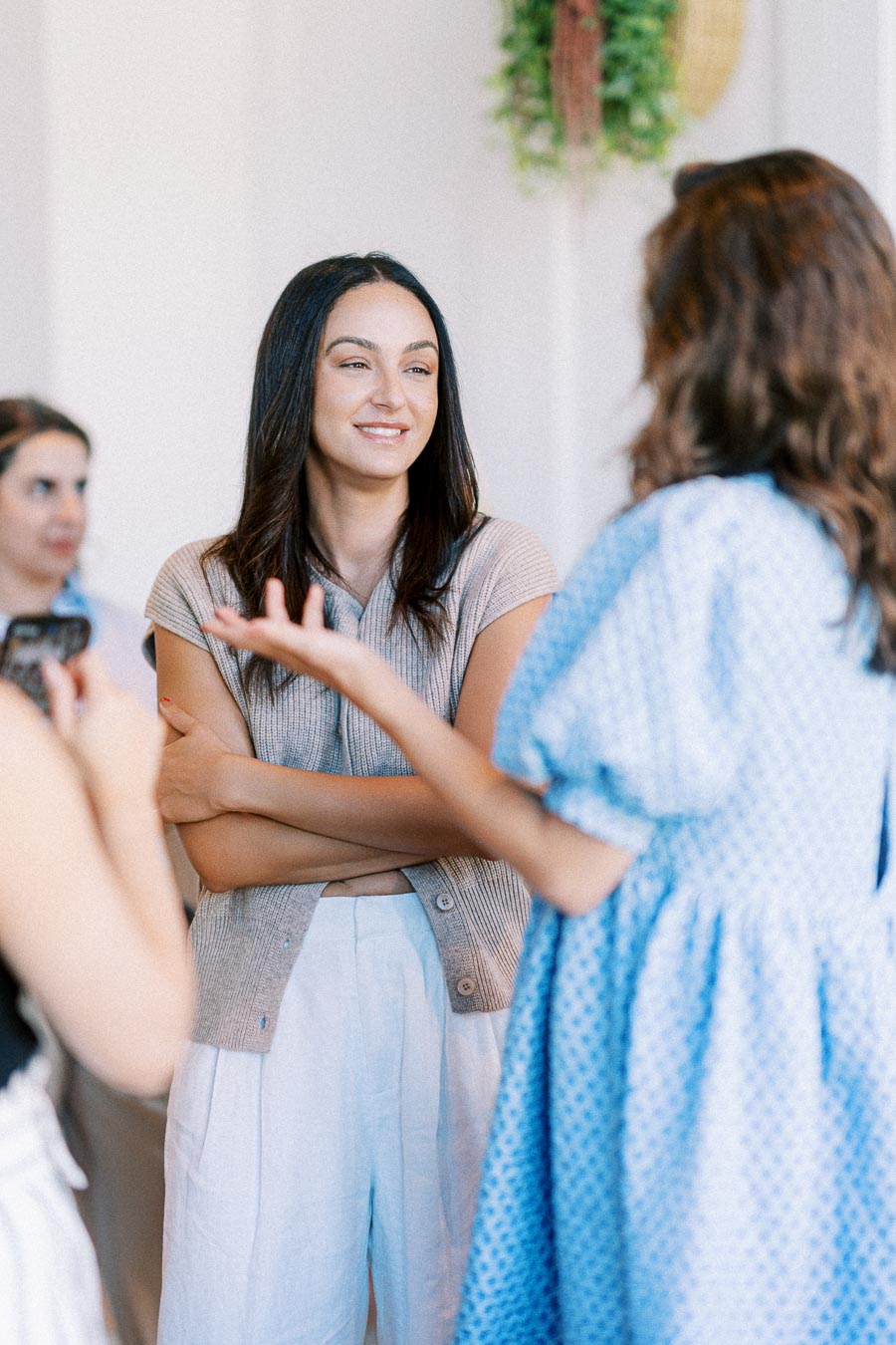 Group of people engaged in a conversation at a social gathering, with a woman in a beige sweater smiling and listening attentively.