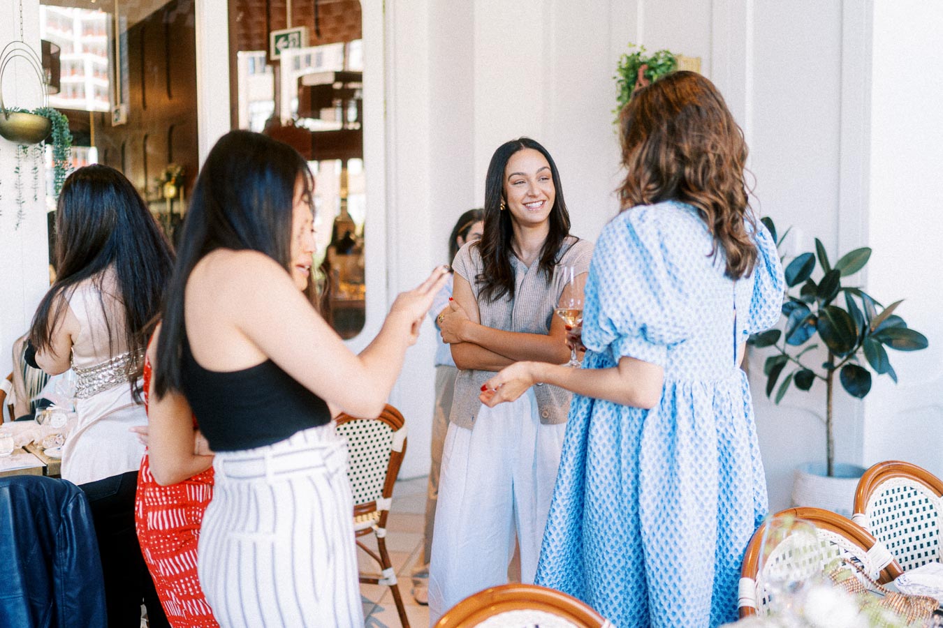 Group of women socializing in a trendy cafe, engaging in conversation and enjoying drinks, with a stylish interior and natural light.