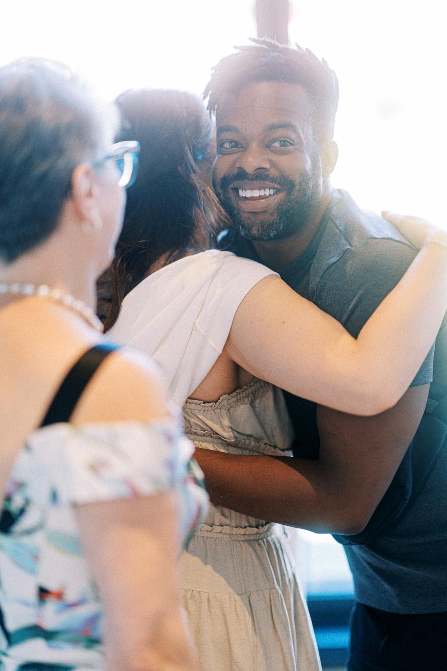 A group of cheerful people sharing a warm embrace and smiling indoors at a social gathering.