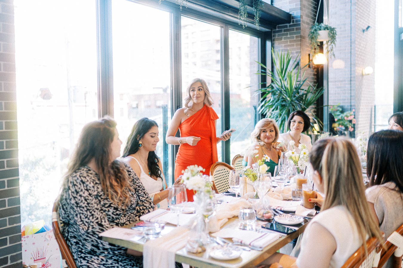 Women enjoying a brunch gathering in a stylish urban restaurant with natural light and greenery.
