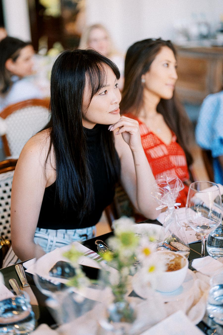 Female guests sitting at a table during an elegant event, surrounded by table settings and floral decor.