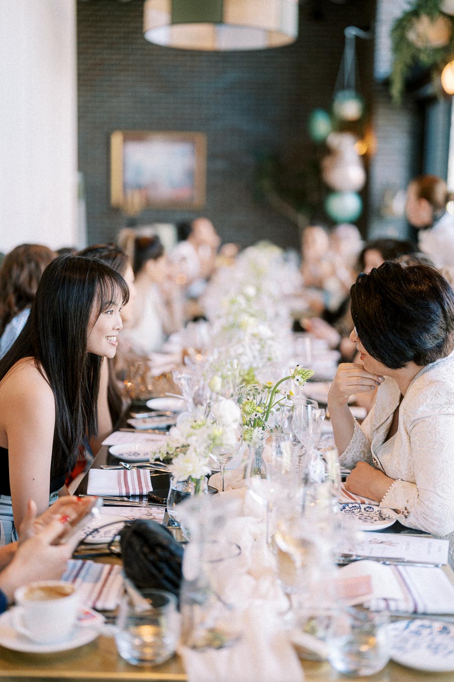 A group of people engaged in conversation at a beautifully decorated dining table set for an elegant event, featuring floral centerpieces and tableware.