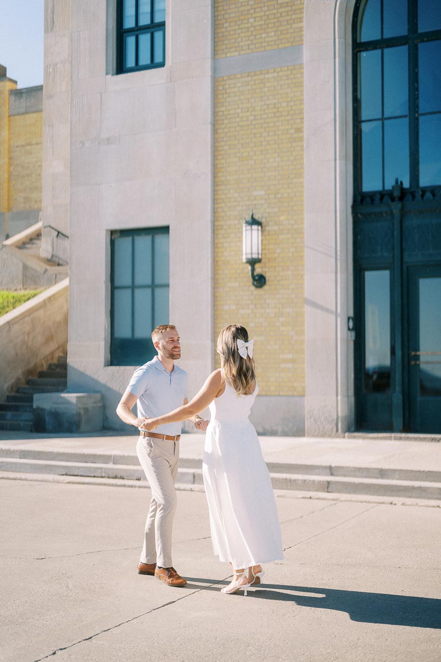 A couple dancing happily outside a historic building on a sunny day, showcasing romantic moments and urban architecture.