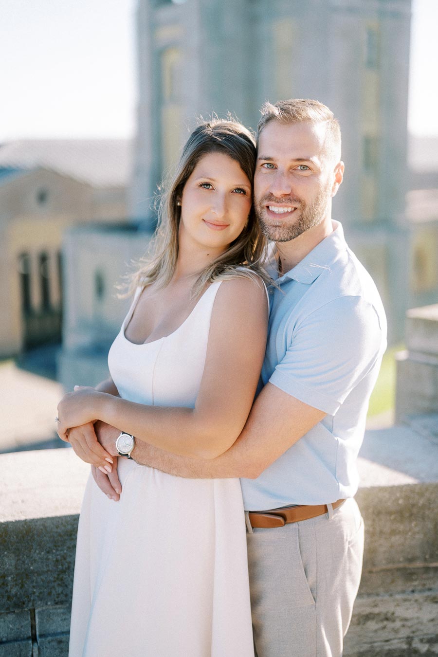 Couple embracing and smiling on a sunny day with a historic building in the background