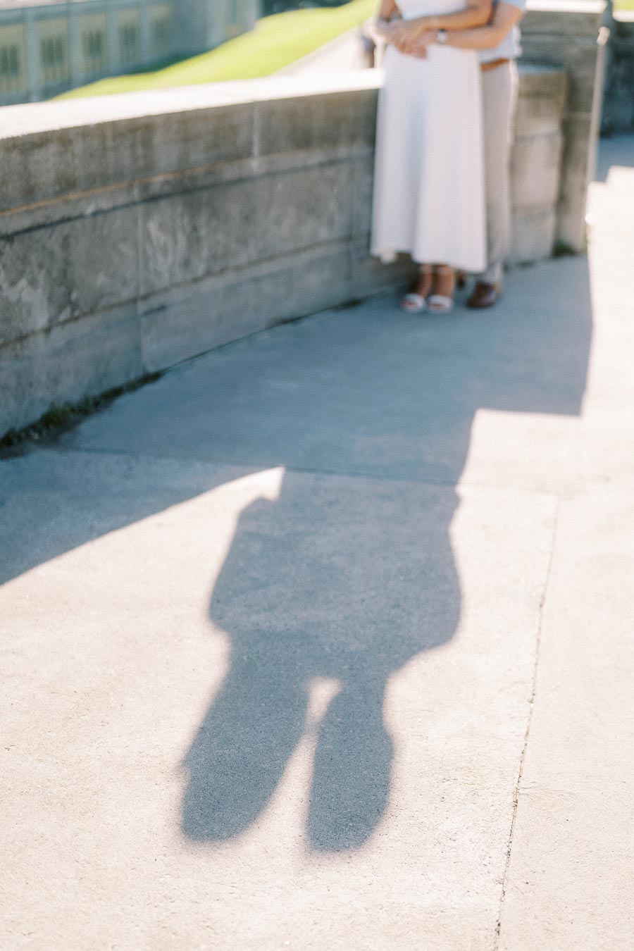 Romantic couple embracing on a sunny day, casting a shadow on a stone walkway.