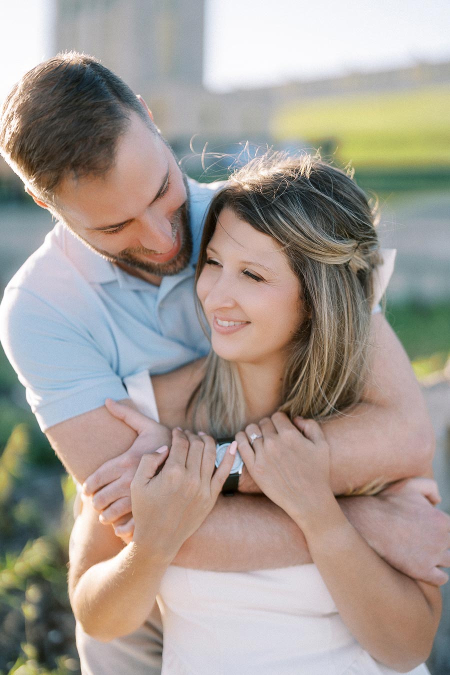 Couple embracing and smiling in a sunny outdoor setting, showcasing love and happiness.