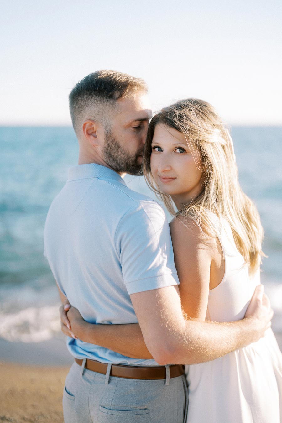 A couple embracing on a sunny beach, with a serene ocean backdrop.
