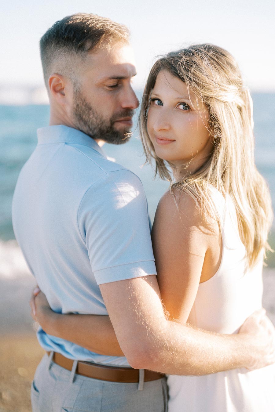 Young couple embracing near the ocean under a clear blue sky, conveying love and togetherness on a sunny day.
