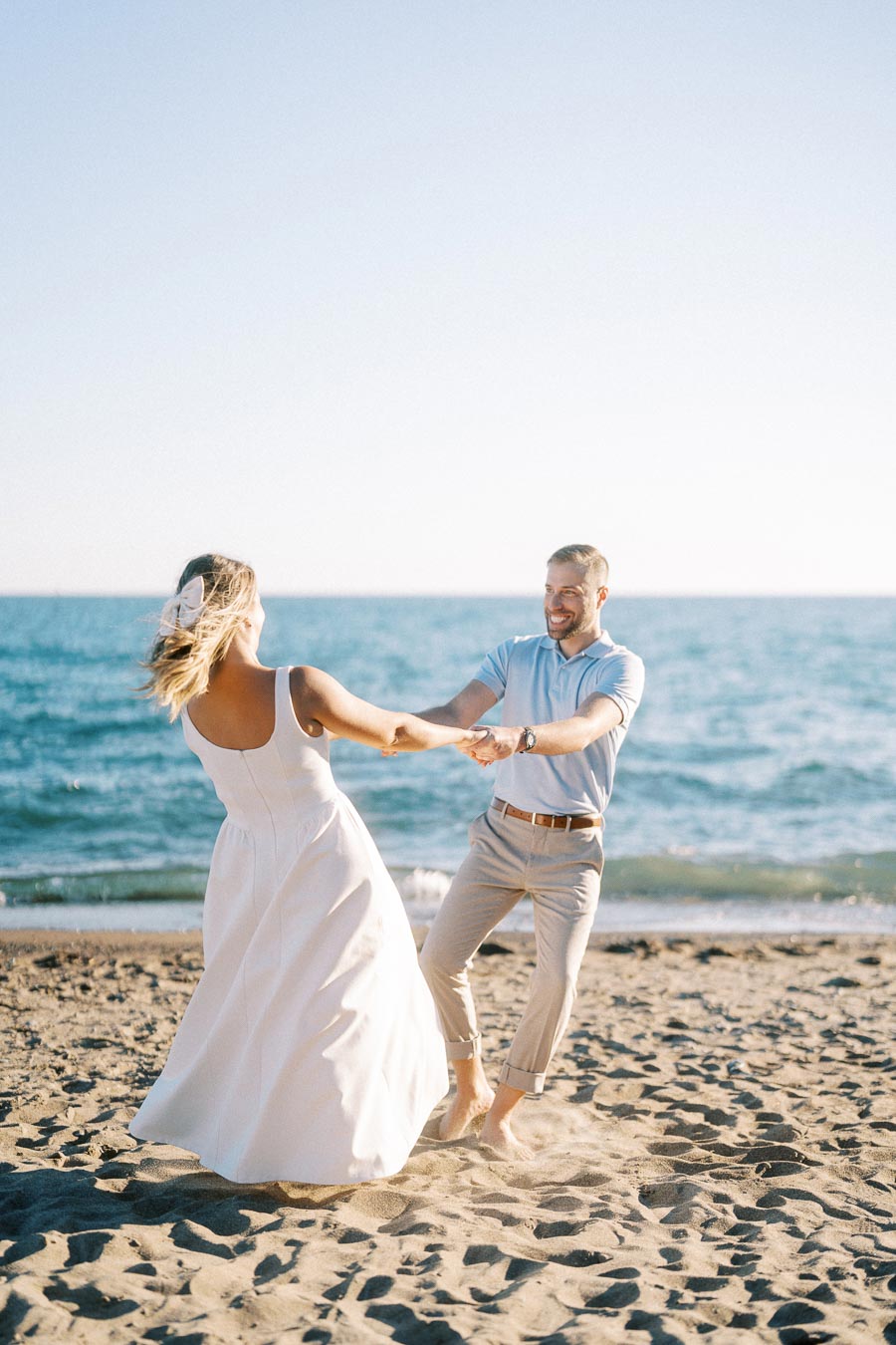 Couple joyfully dancing on a sunny beach, with a blue ocean in the background and clear sky above, capturing a moment of happiness and romance.