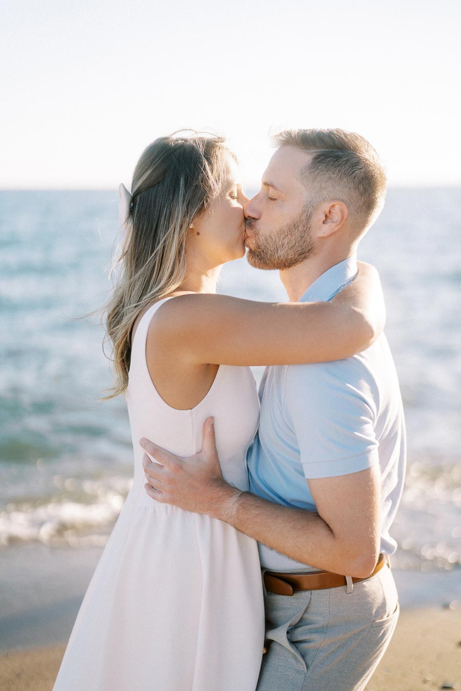 A couple kissing on a sunny beach, expressing romance and affection, with the ocean in the background.
