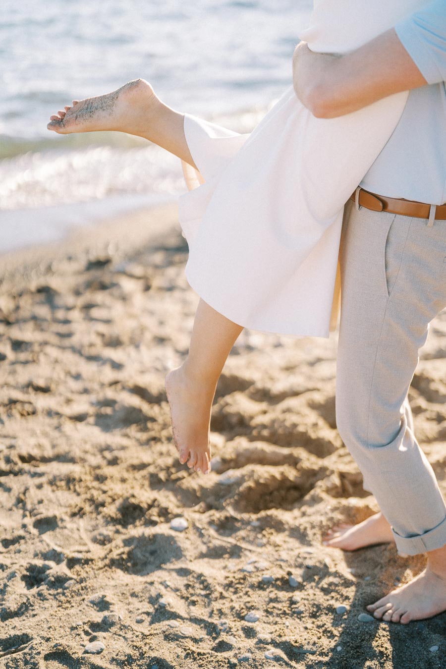A couple sharing a joyful moment on a sunny beach, with the man playfully lifting the woman, capturing the essence of a romantic seaside escape.