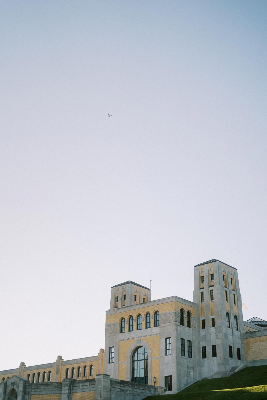 Historic building with towers under a clear blue sky, featuring arched windows and stone architecture with a small airplane flying in the distance.