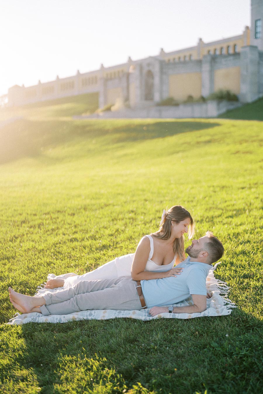 A couple relaxing on a picnic blanket in a sunny park with green grass, enjoying a serene moment together during a summer day.