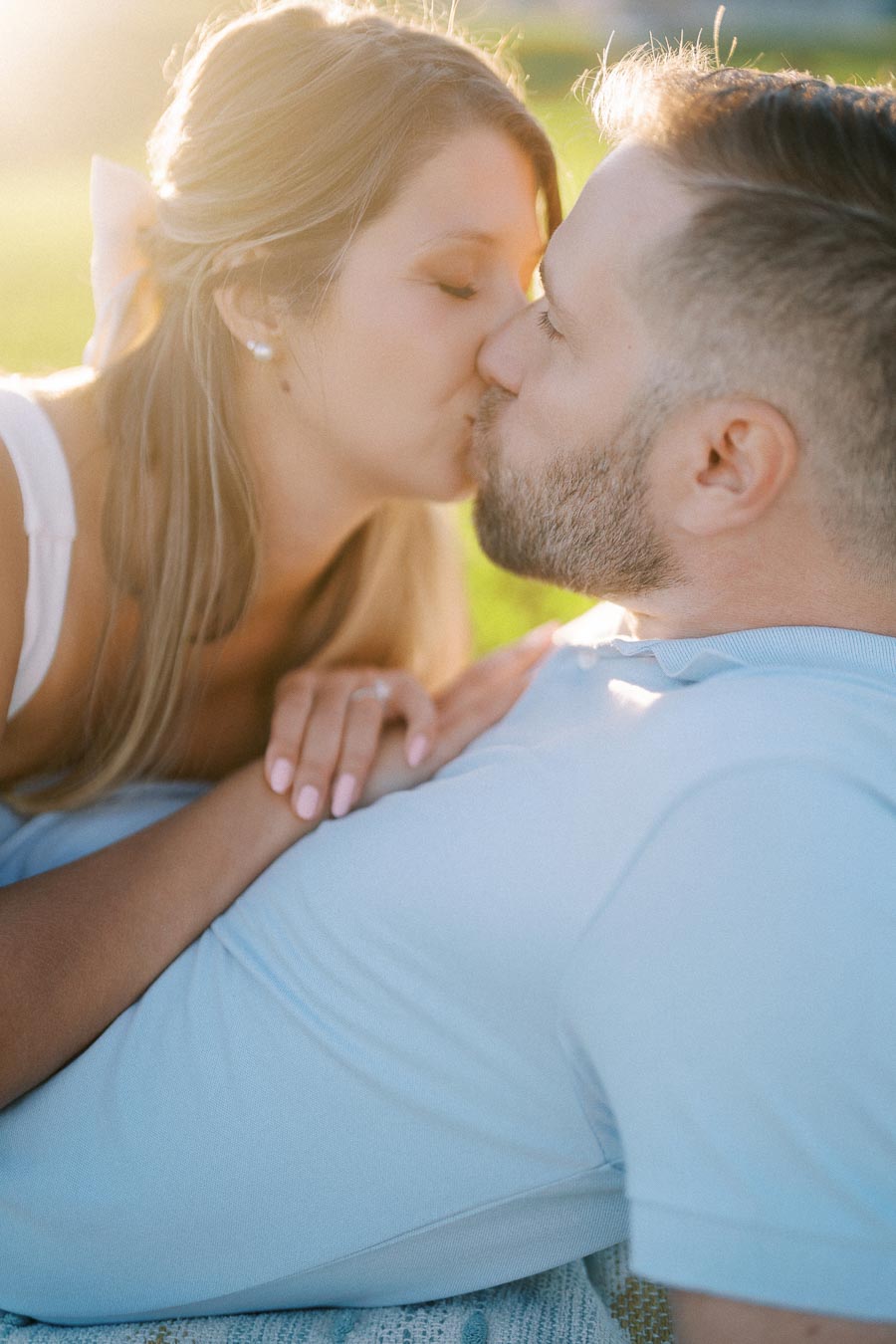 A couple sharing a romantic kiss in a sunlit outdoor setting.