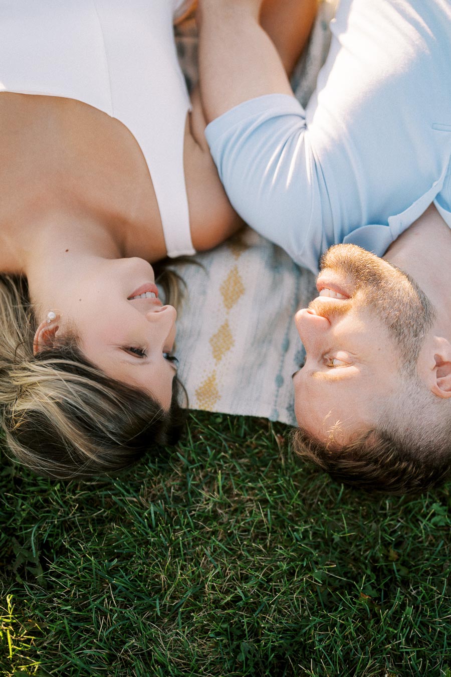 A couple lying on a picnic blanket in the grass, gazing into each other's eyes, capturing a romantic outdoor moment.