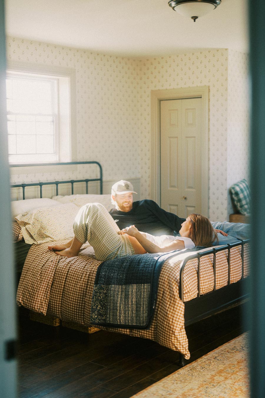 Sunny bedroom scene with a couple relaxing on a checkered bedspread, featuring a cozy atmosphere and vintage decor.