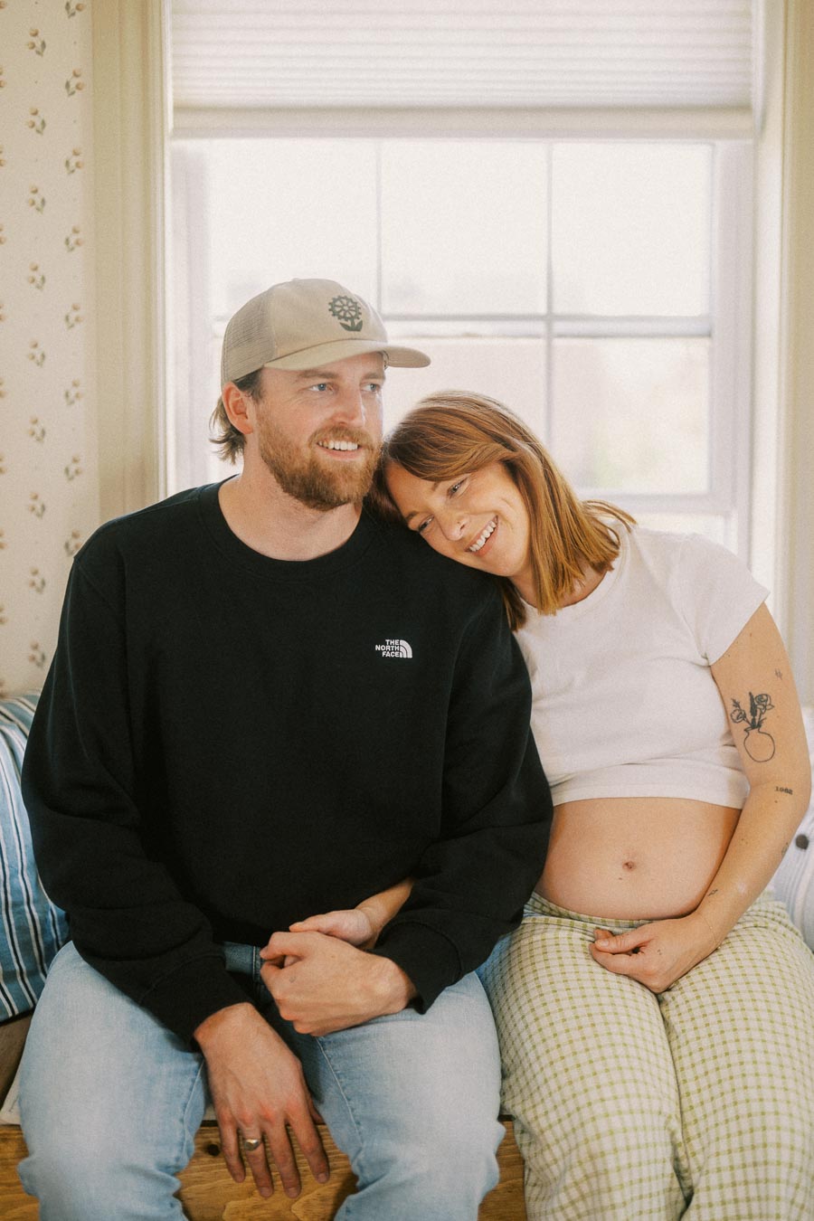 A happy couple sitting together in a cozy room, with the woman showing her baby bump, expressing joy and anticipation.