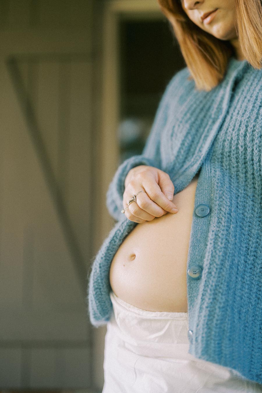 A pregnant woman gently touching her baby bump, wearing a cozy blue sweater to emphasize warmth and comfort during maternity.