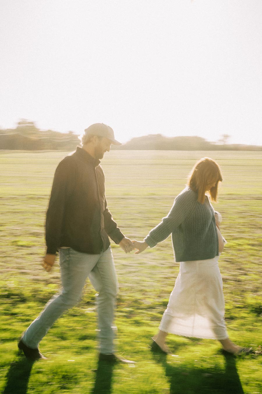 A couple holding hands and walking in a sunlit field, with soft-focus lighting creating a warm and serene atmosphere.