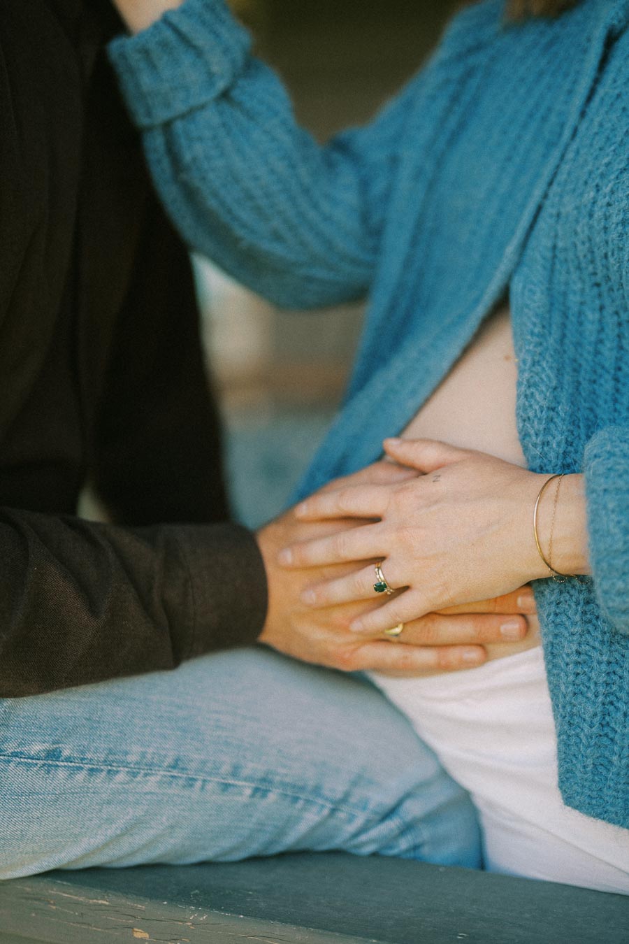Hands on pregnant belly with couple in cozy sweaters, symbolizing love and expectation.
