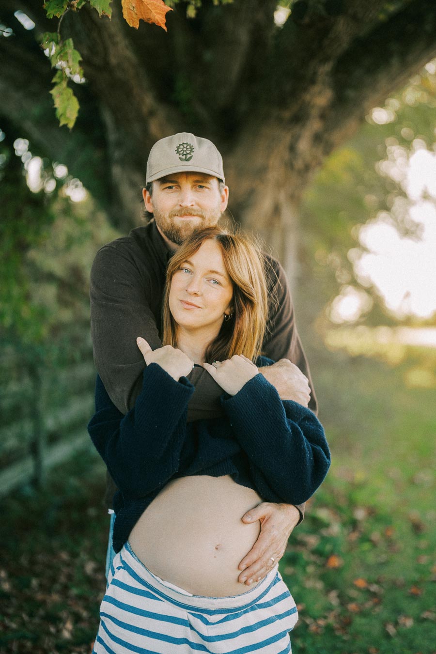 A couple embracing in a serene outdoor setting, with a focus on the woman's pregnant belly, symbolizing love and anticipation.