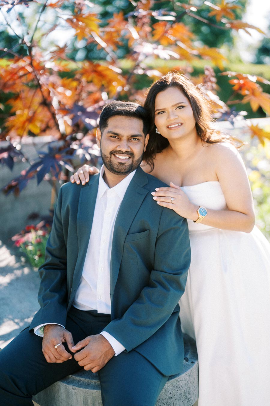 Young couple posing in formal attire, with autumn foliage in the background, highlighting a romantic moment outdoors.